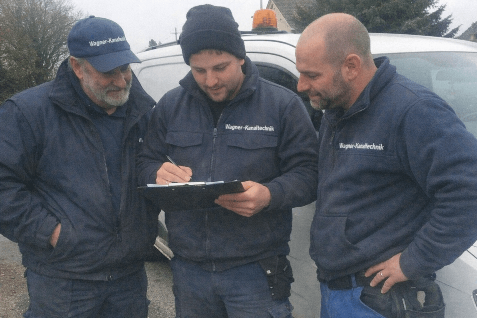 Zwei Servicetechniker prüfen vor einem Einsatzfahrzeug einen Plan, im Hintergrund Werkzeugkoffer und Schutzkleidung